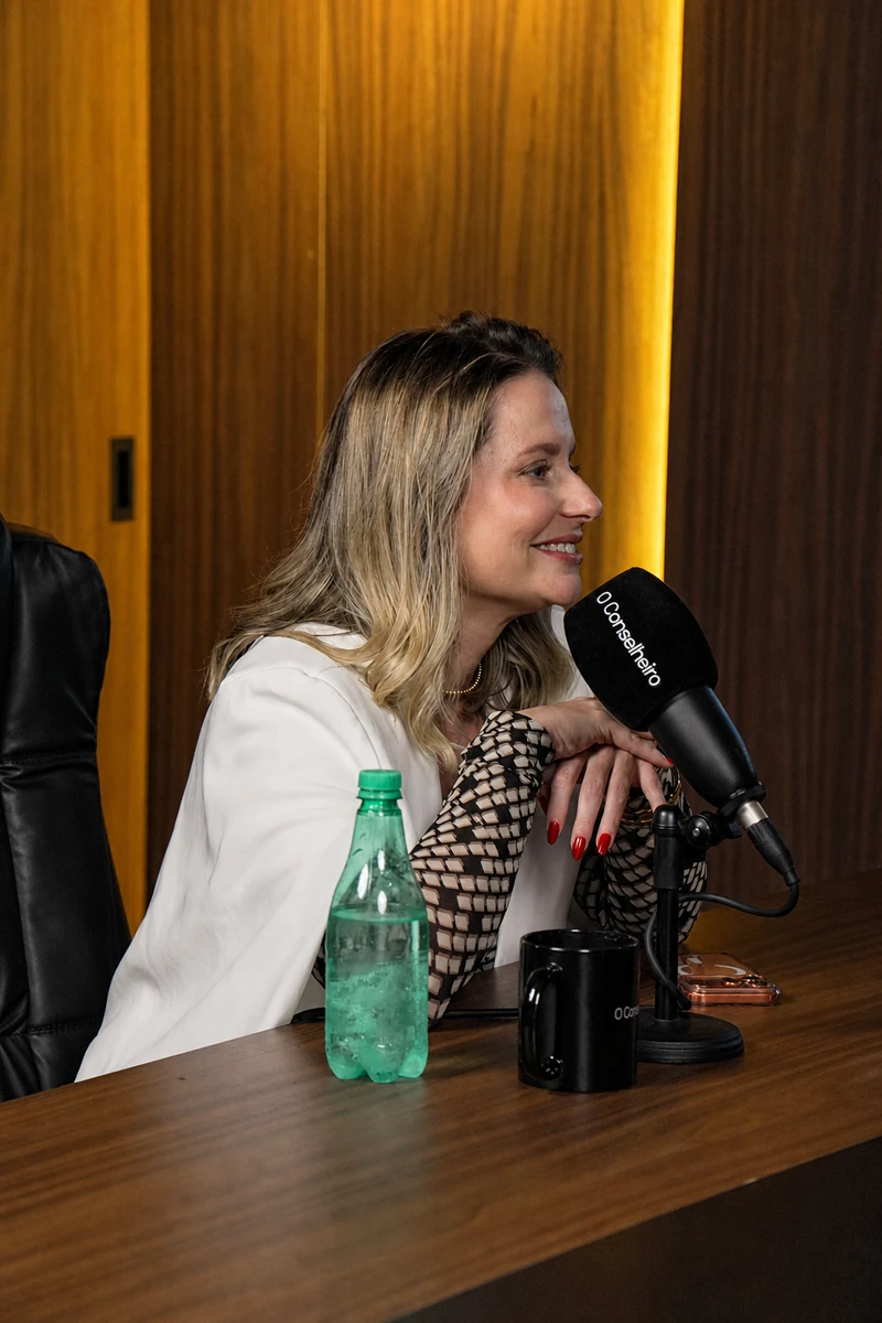 Paula Angelini sorrindo ao microfone, na gravação de um podcast