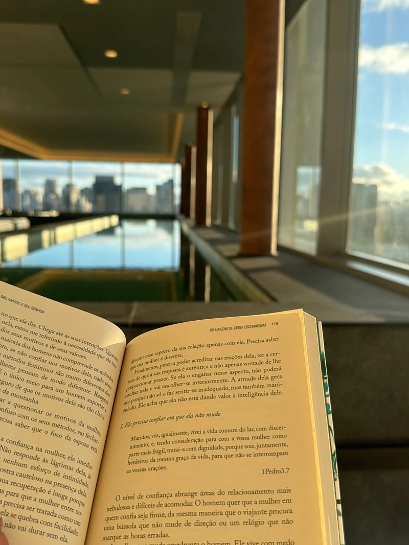 Livro aberto nas mãos de Paula Angelini, diante de uma piscina com vista para a cidade